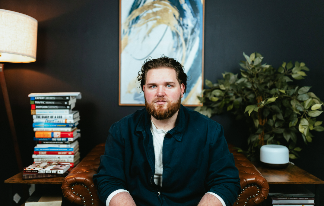 Jed Smith seated in a leather armchair with a stack of leadership books beside him